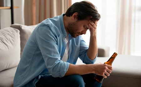 Мужчина сидит на диване держа бутылку алкоголя
